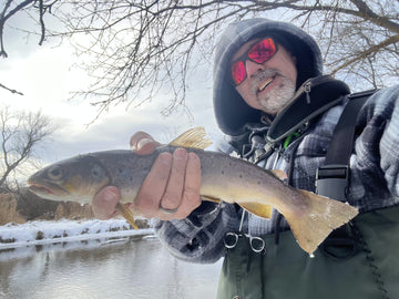 Man holding a fish by a snowy river