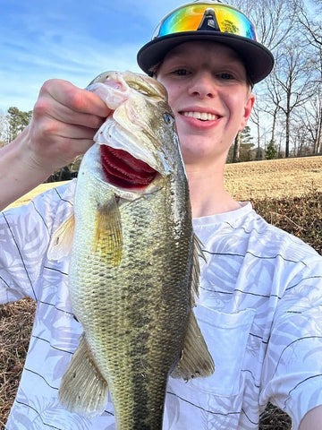 Person holding a large bass fish outdoors on a clear day