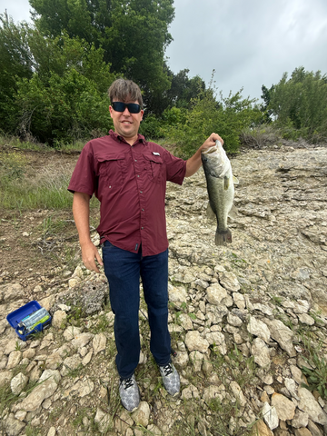 Man holding a fish on a rocky landscape with trees in the background