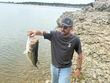 Man holding a fish by a lake with rocky shore